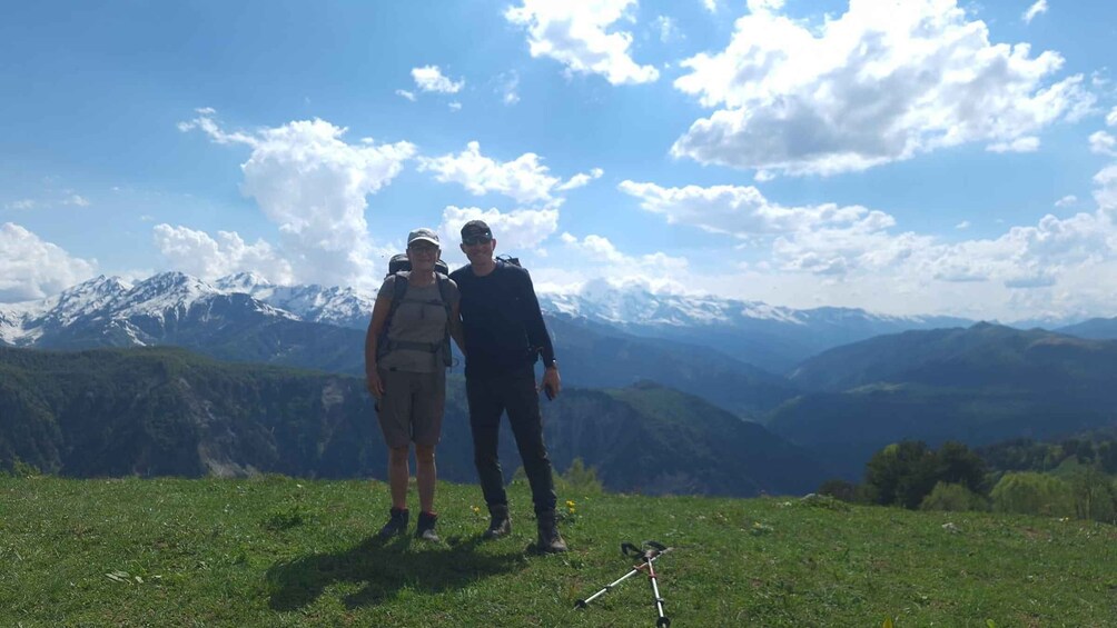 Two people standing on a grassy hill with a mountain range in the background. 1
