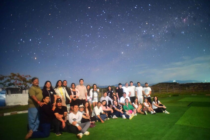 A group of people posing on a grassy field under a starry night sky. 2