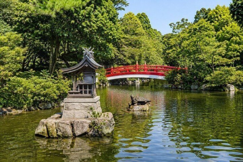 Un jardín japonés tradicional con un farol de piedra, un pequeño puente y un puente rojo al fondo. 3