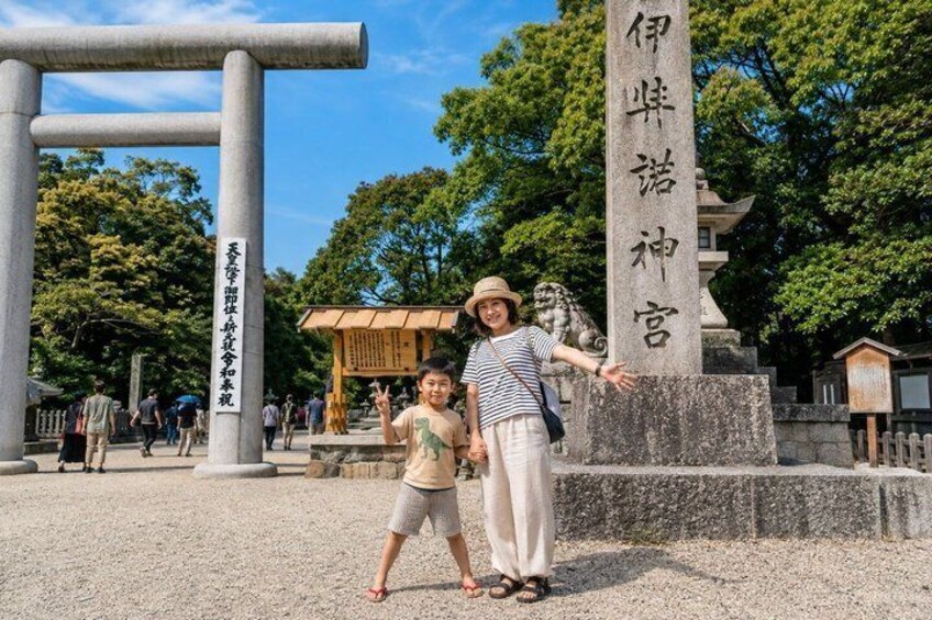 Un monumento de piedra con caracteres japoneses, un gran torii y un edificio tradicional japonés al fondo. 1