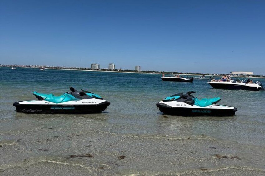 Two jet skis on a clear beach with a city skyline in the background. 5