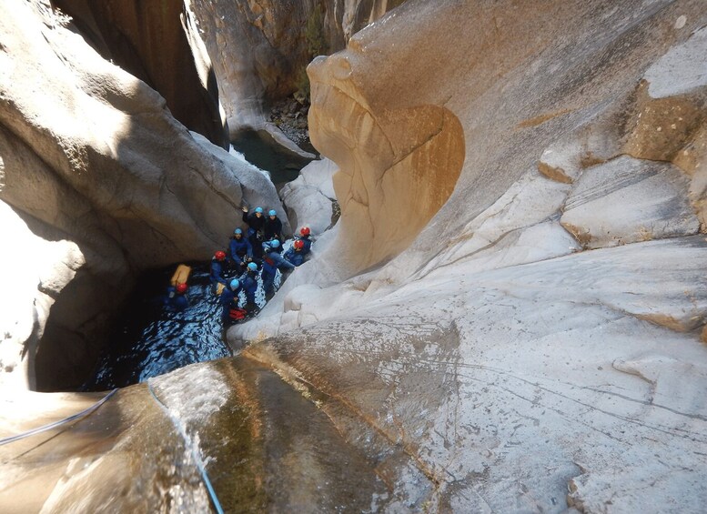 A group of people in blue jackets and helmets navigating a narrow canyon with a river. 2