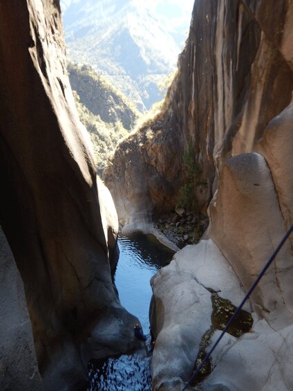 A narrow canyon with a small stream, rocky walls, and distant mountains. 5