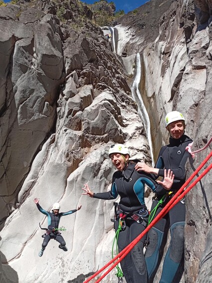 A person rappelling down a rocky cliff with a waterfall in the background. 1
