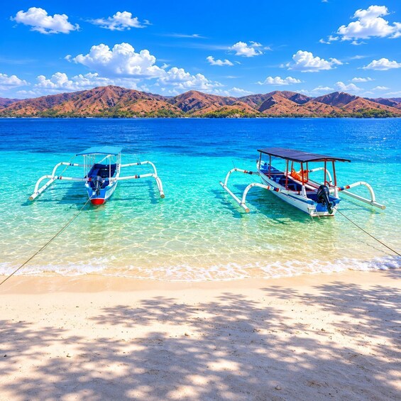 Two traditional boats anchored on a clear turquoise beach with mountains in the background. 1