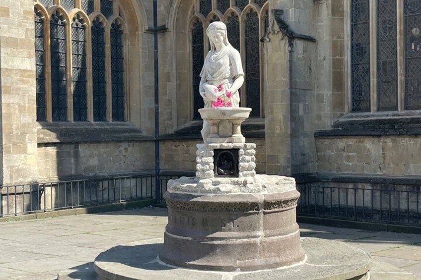 A stone statue of a woman holding flowers in front of a church with arched windows. 5