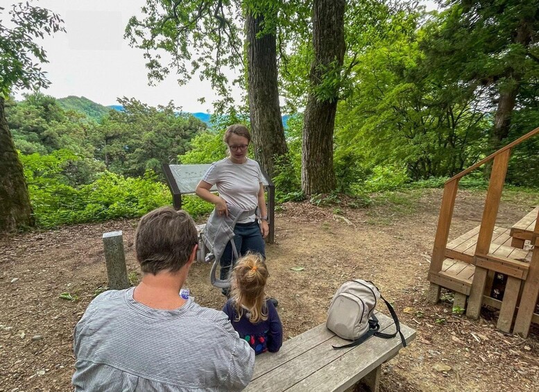 A person standing on a wooden platform, a child sitting on a bench, and a backpack on the ground. 5