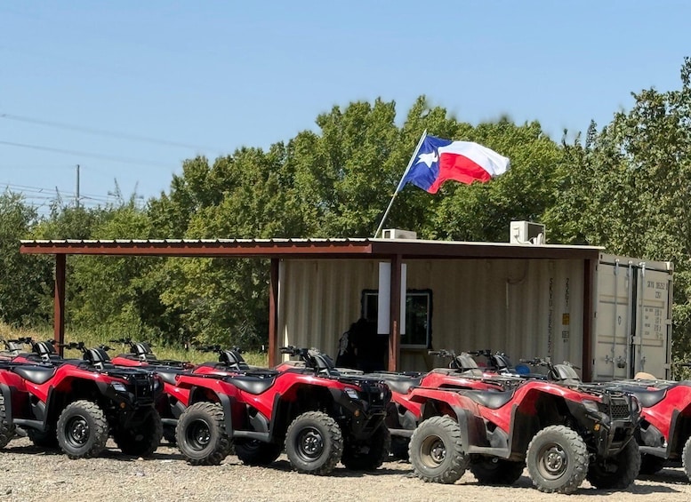 A row of red ATVs parked in front of a small building with a Texas flag. 3