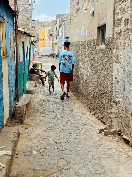 A narrow cobblestone street with buildings on either side, one with a blue door and another with a mural. 3