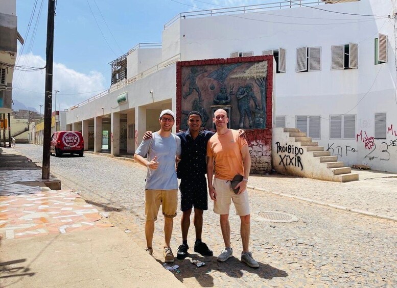 Three people standing on a street with a mural and graffiti on the buildings. 2