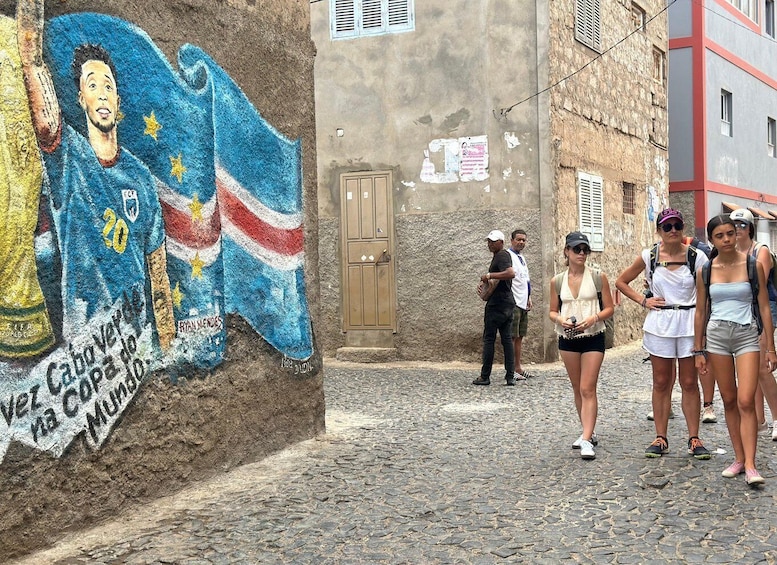 A mural of a soccer player on a wall, a cobblestone street, and people walking. 4
