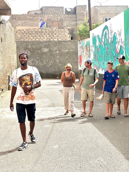A group of people walking on a street with a mural in the background. 1