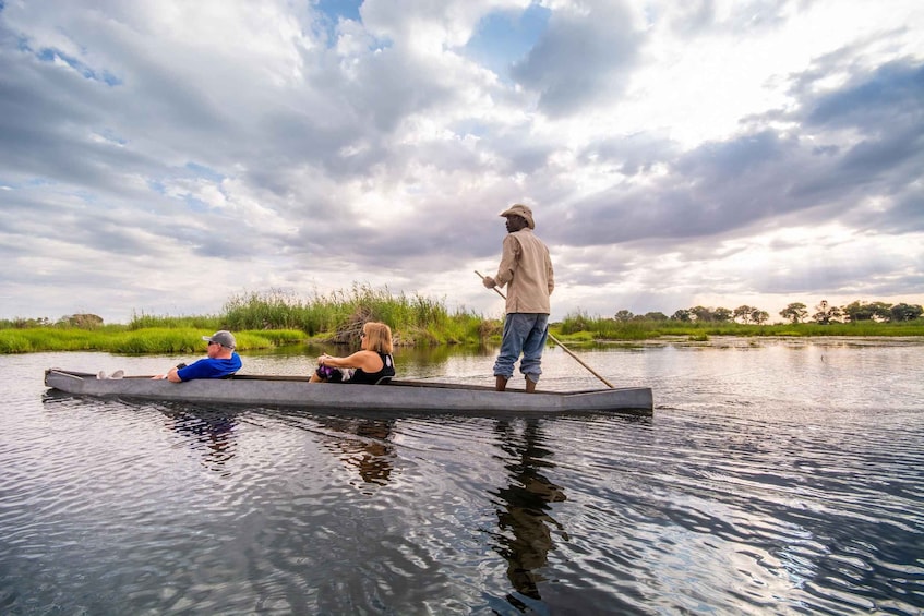 Three people on a narrow waterway, one standing and two seated, with a cloudy sky above. 3