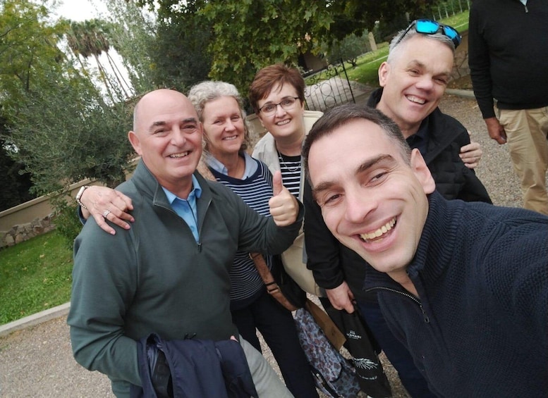 A group of people outdoors, possibly in a park or garden, with trees and a paved path in the background. 3