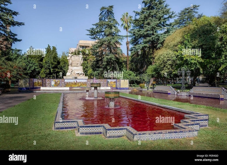 A square pool with a statue in the center, surrounded by trees and a tiled walkway. 1