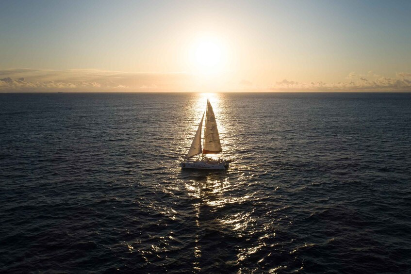 Ein Segelboot auf ruhigem Wasser, im Hintergrund geht die Sonne unter. 1