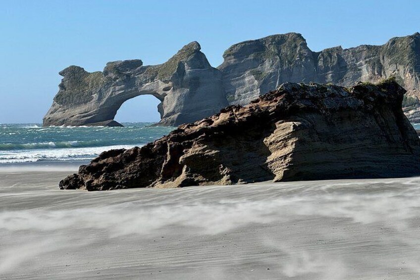 A coastal landscape with a prominent rock formation featuring an arch. 2