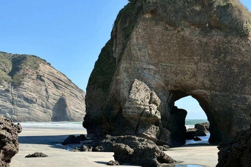 A large rock arch formation on a beach with a clear sky. 2