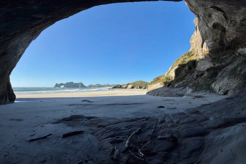 A beach with a natural rock arch, sandy shore, and distant rocky formations. 5