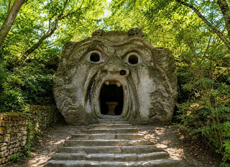 A stone structure resembling a face with eyes and mouth, surrounded by greenery and a stone wall. 3