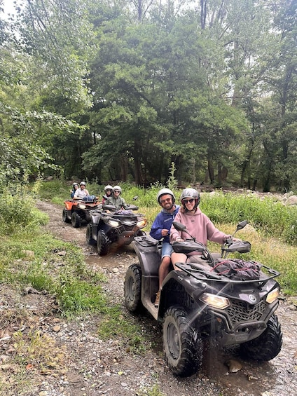 Four people on ATVs on a dirt path surrounded by trees. 1