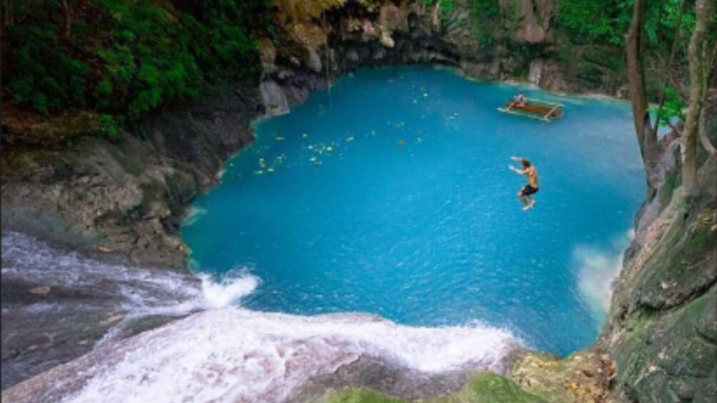 A person jumping into a clear blue pool surrounded by rocky cliffs and lush greenery. 2
