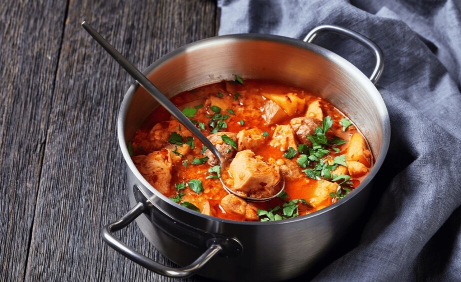A pot of stew with chunks of meat and vegetables, garnished with herbs, on a wooden surface. 4