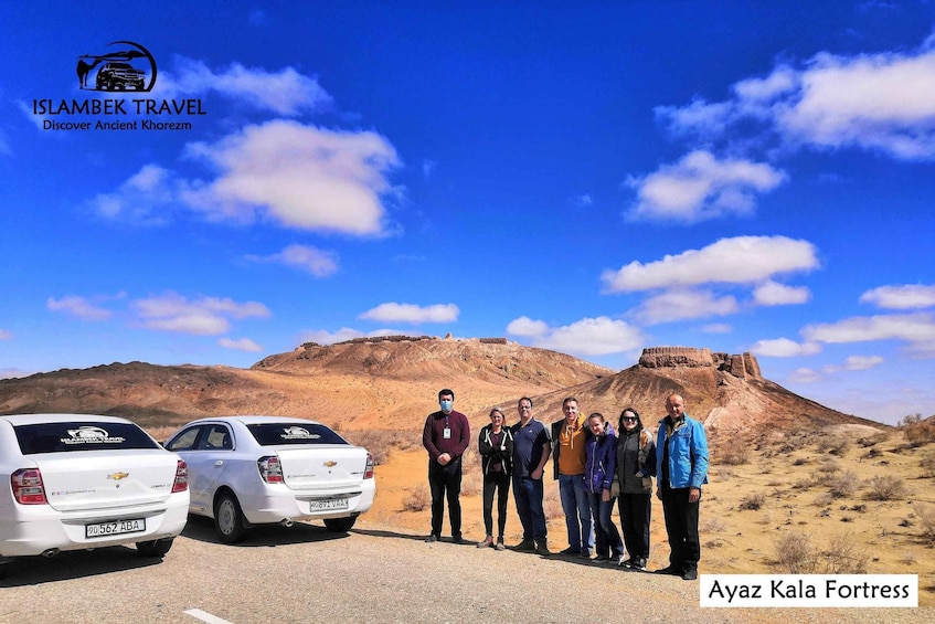 A group of people standing in front of Ayaz Kala Fortress with two white cars parked nearby. 5