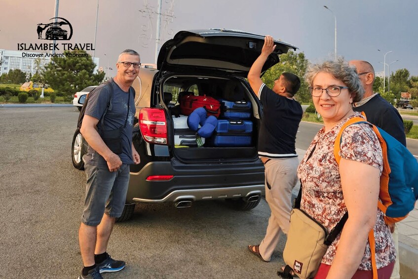 A group of people standing beside a vehicle with its trunk open, luggage visible inside. 2