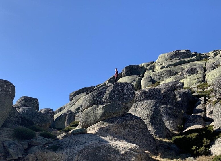 A person standing on a rocky outcrop with a clear blue sky above. 3