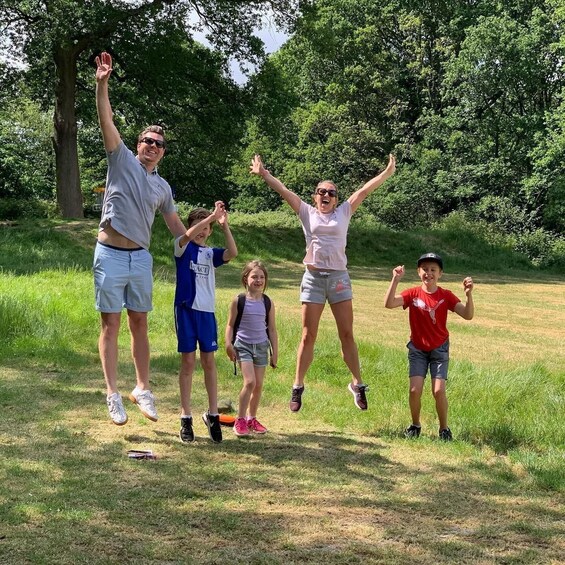 A family of five jumping in a grassy field with trees in the background. 2
