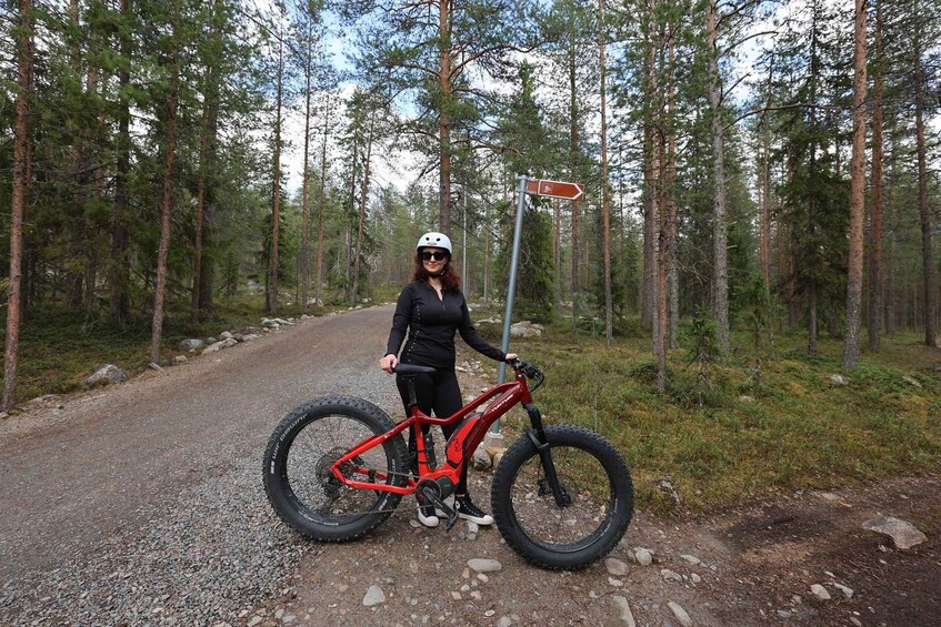 A person standing next to a red mountain bike on a gravel path in a forested area. 4