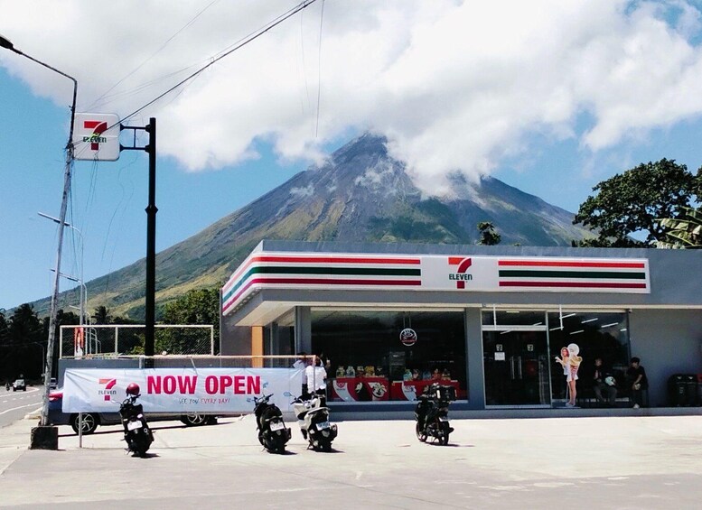 A 7-Eleven convenience store with a banner stating 'NOW OPEN' and several motorcycles parked in front. 4