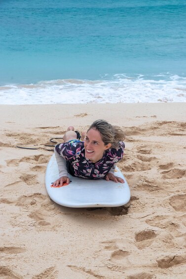 A person lying on a surfboard on a sandy beach with the ocean in the background. 5