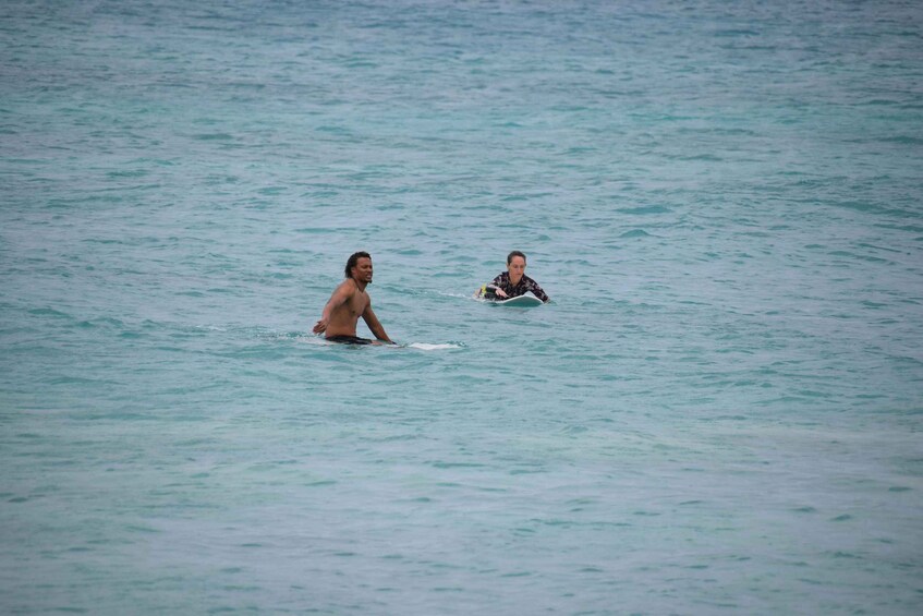 Two people in the ocean, one standing and one lying on a surfboard. 2