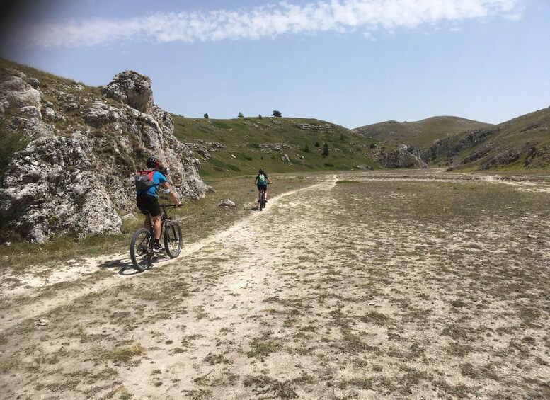 Two cyclists on a dirt path with rocky terrain and sparse vegetation. 5