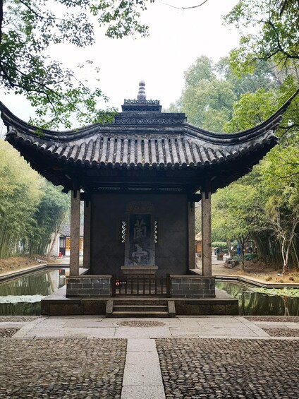 A traditional Chinese pavilion with a curved roof, surrounded by a pond and bamboo trees. 2