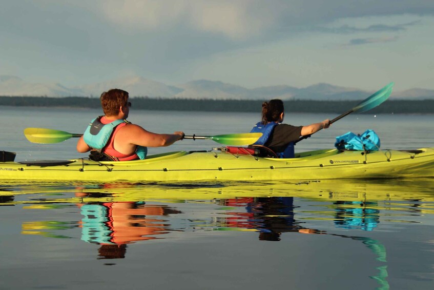 Two people kayaking on a calm lake with mountains in the background. 4