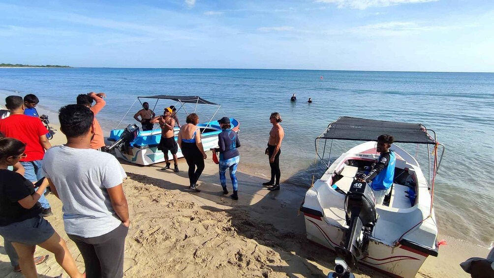 A group of people on a beach with boats and a clear sky. 2