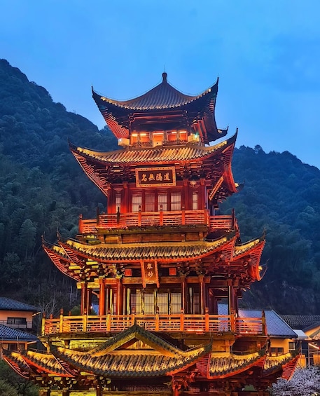 A multi-tiered traditional Chinese pagoda with illuminated red and gold detailing, set against a backdrop of lush green hills. 5