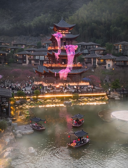A traditional multi-tiered pagoda with pink floral decorations, surrounded by a pond with boats and a crowd of people. 3