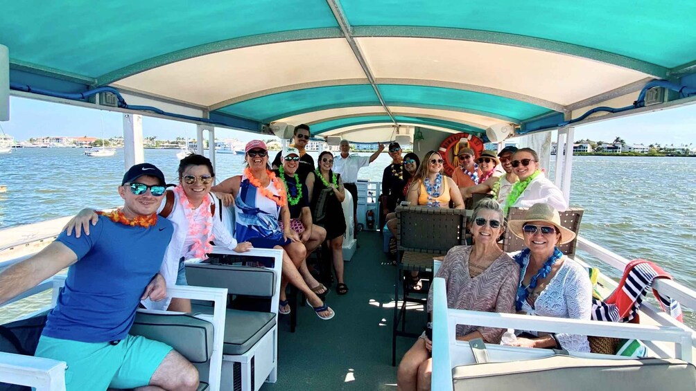 A group of people on a boat with a covered deck, surrounded by water and buildings in the background. 2