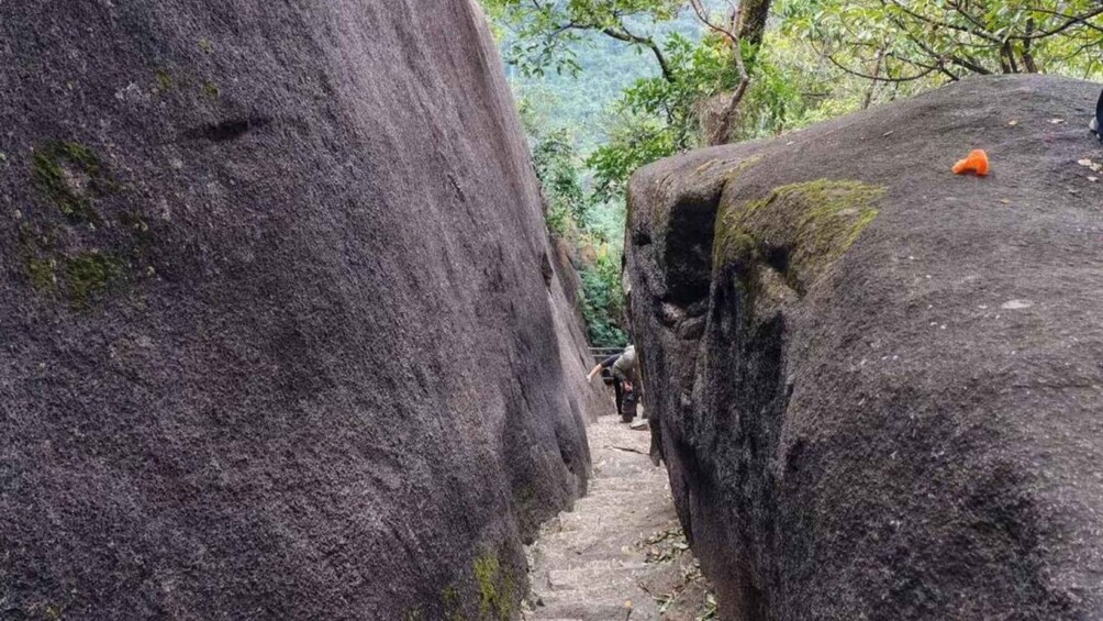 A narrow stone pathway between large boulders in a forested area. 5