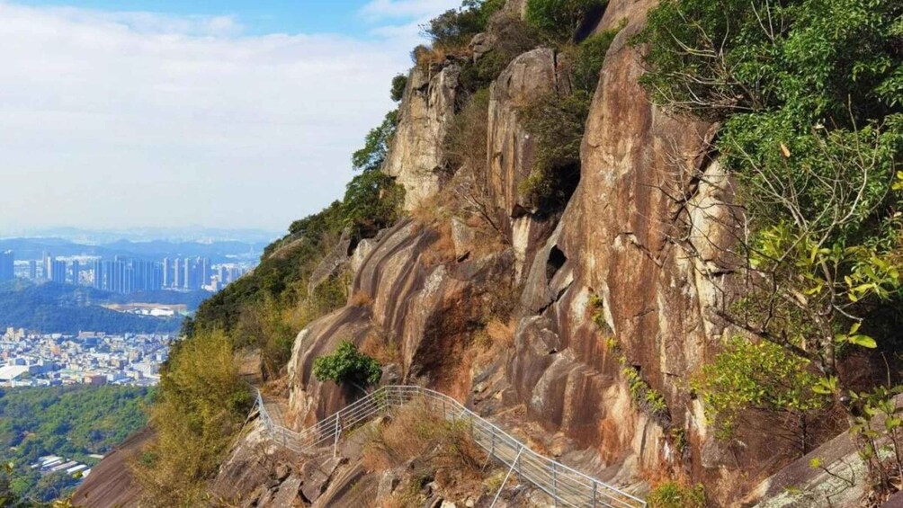 A rocky mountain with a metal staircase and a cityscape in the background. 3