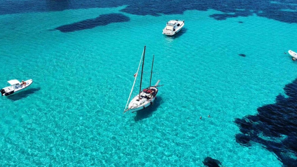 A sailboat anchored in clear turquoise waters with other boats nearby. 4