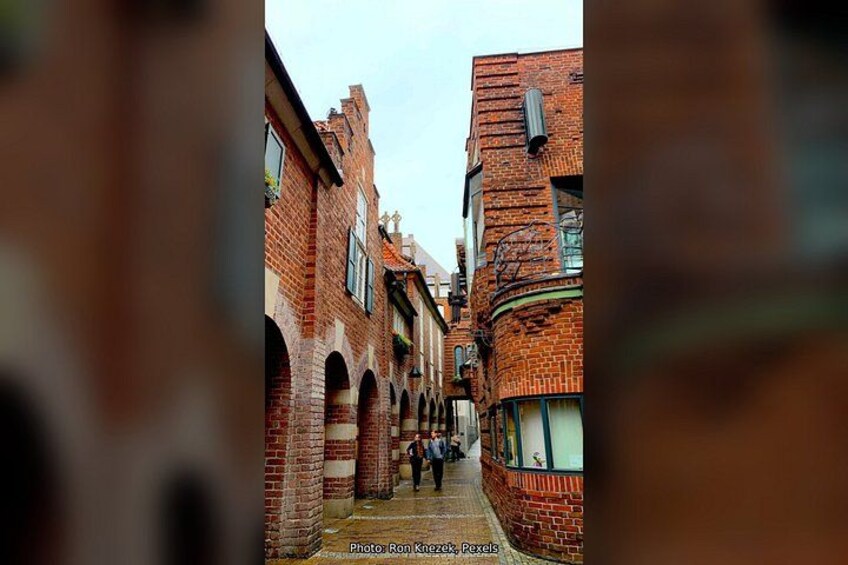 A narrow alley with brick buildings, arched doorways, and a person walking. 5