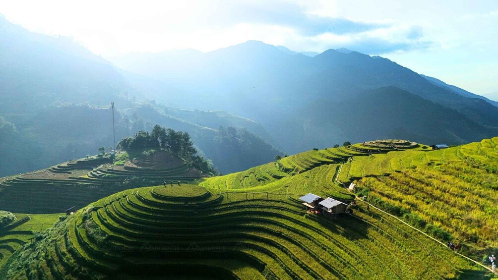 Terraced rice fields, a small building, and mountains in the background. 2