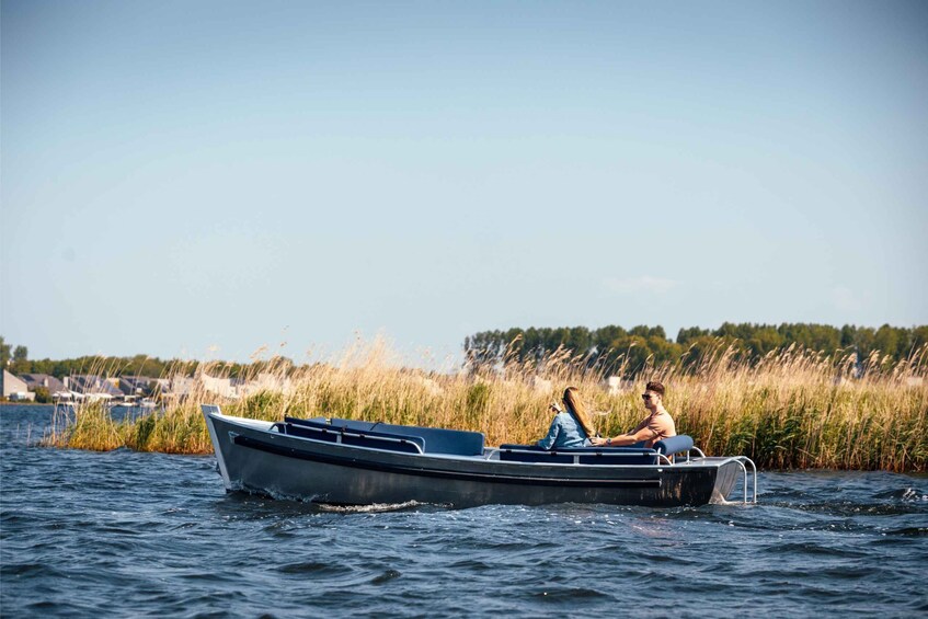 A small motorboat on calm water with two people, surrounded by tall grass and a clear sky. 5