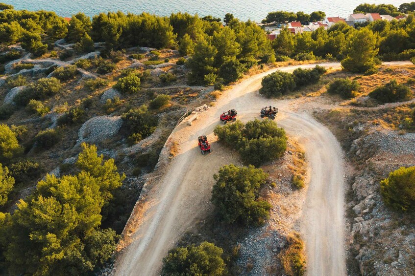 A dirt road winding through a hilly landscape with dense greenery and a coastal area in the background. 4