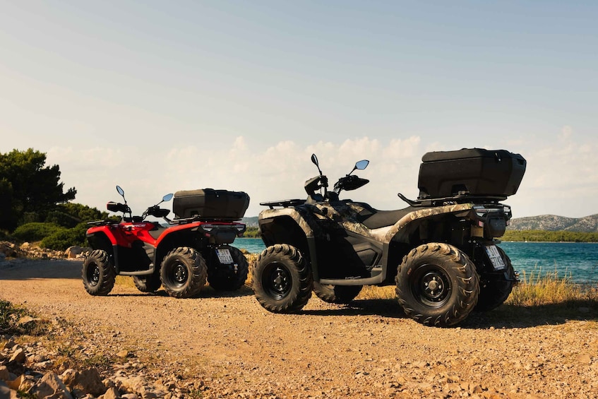 Two ATVs parked on a gravel path by a body of water with mountains in the background. 1